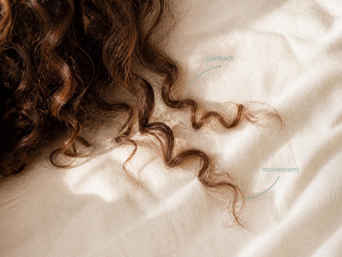 Close view of textured hair resting and moving across a pillow surface during sleep.